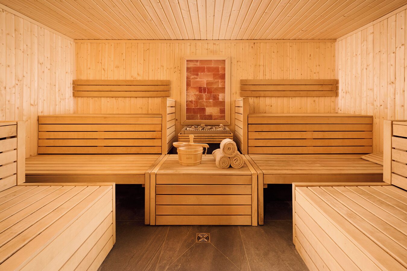 A sauna with wooden benches and a central table with towels and a bucket.