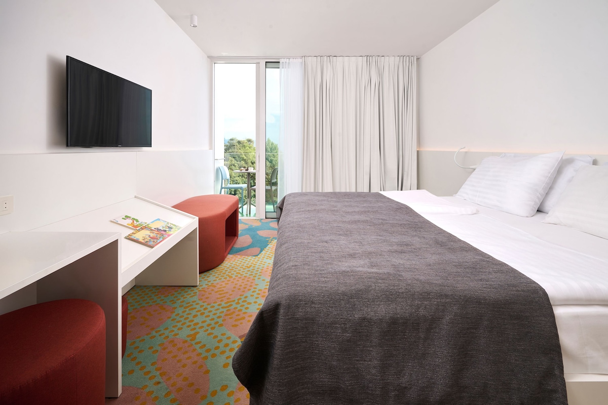 A hotel room with a bed, a desk, a chair, and a television.