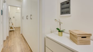 A hallway with a wooden floor, white walls, and a white counter with a plant and a wooden box. - Rooms Vidar Train station (Mestre)