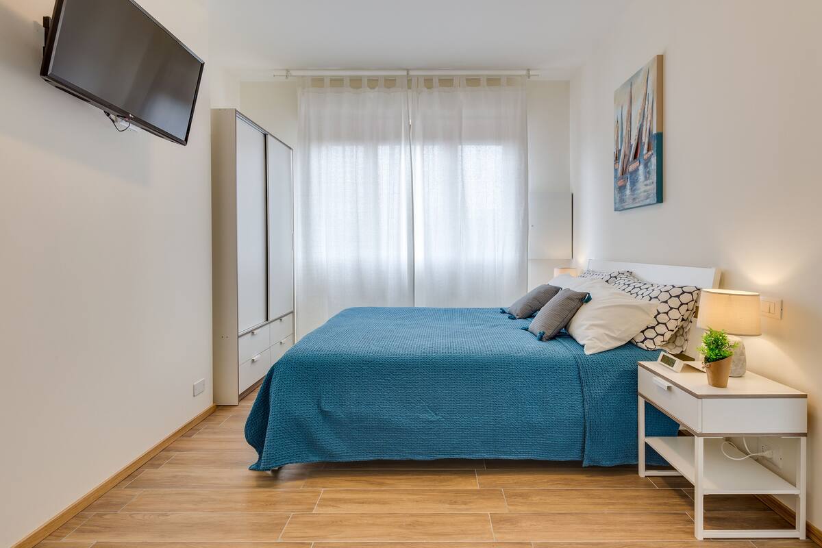 A bedroom with a bed, bedside table, lamp, and a painting on the wall.