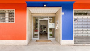 A building entrance with a glass door, a blue and orange facade, and a sign indicating a public service. - Rooms Vidar Train station (Mestre)