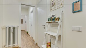 A hallway with white walls, a radiator, a white shelf with items, and a door leading to another room. - Rooms Vidar Train station (Mestre)