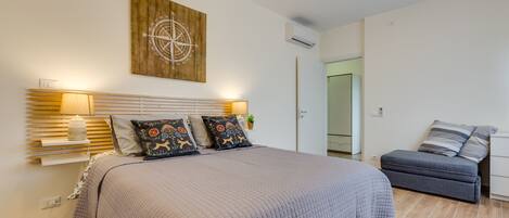 A bedroom with a large bed, bedside lamps, a wooden headboard, and a wall-mounted compass decoration.