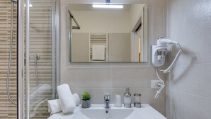 A bathroom with a glass-enclosed shower, a white sink, a mirror, and a hairdryer on the wall. - Rooms Vidar Train station (Mestre)