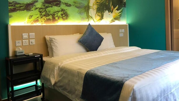 Een hotelkamer met een bed, een nachtkastje, een wandlamp en een muurschildering van een tropisch landschap.