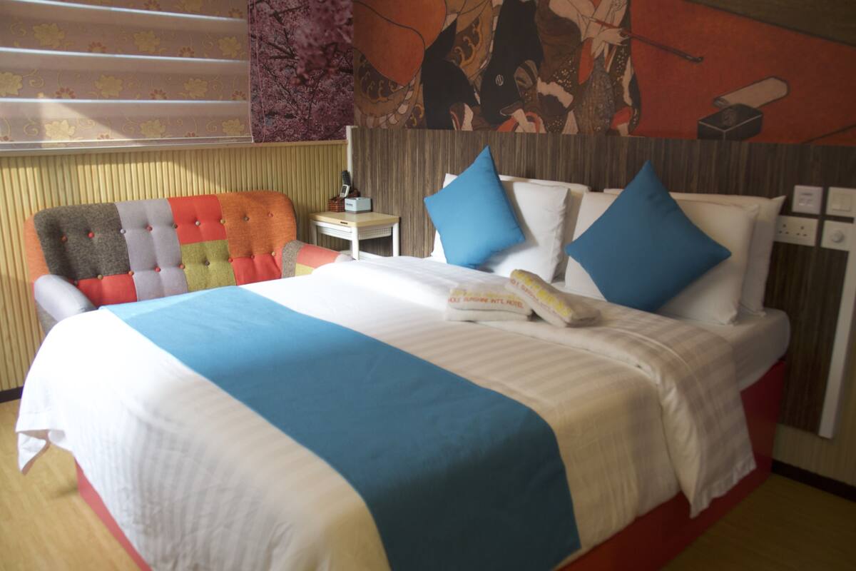 Ein Hotelzimmer mit einem großen Bett, mehreren Kissen, einem Nachttisch mit Lampe und einer Wand mit Blumenmuster.