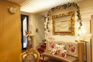 A room with a large ornate mirror, a bench with floral cushions, and a staircase with red carpet. - Hotel Astigiana (Varazze)