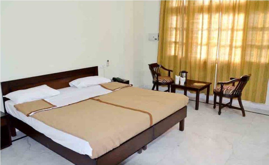 A hotel room with a bed, a desk, two chairs, and a window with curtains.