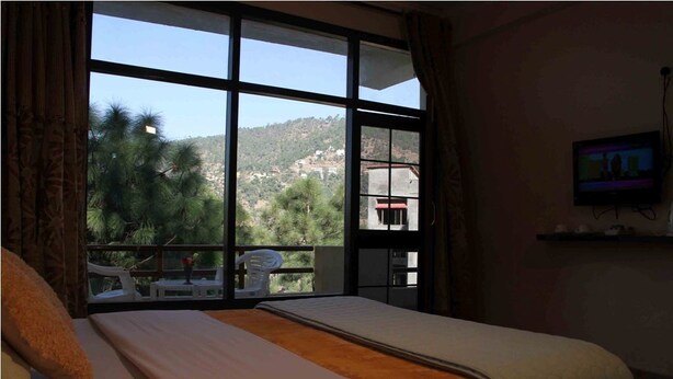 A hotel room with a large window, a bed, a television, and a balcony with a chair.