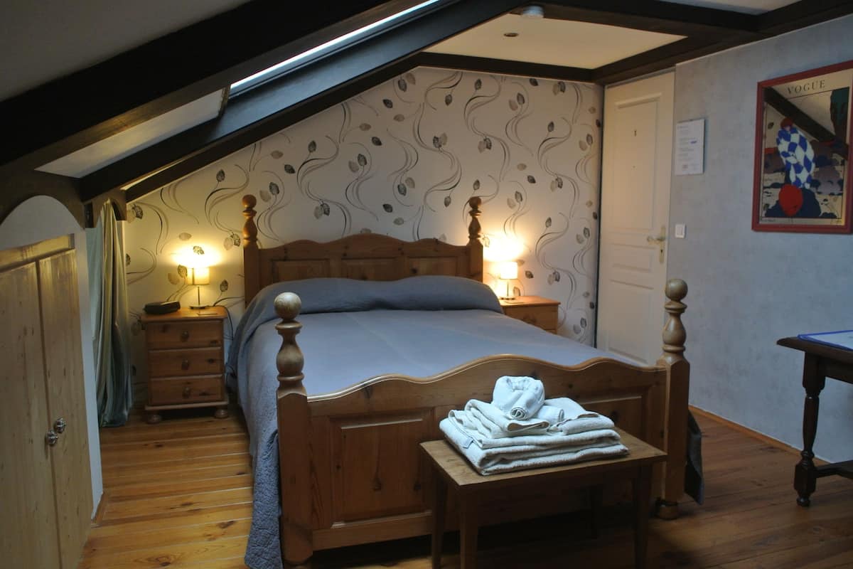 Une chambre avec un lit en bois, deux tables de chevet avec des lampes, un banc en bois avec des serviettes et un papier peint à motifs.