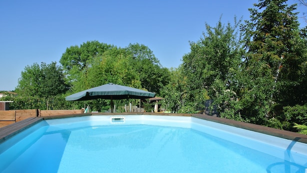 Una piscina rectangular con un deck de madera que la rodea, un área de estar cubierta y abundante vegetación al fondo.