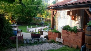 Un espacio al aire libre rústico con una estructura de madera, un camino de grava y un pequeño jardín con macetas.