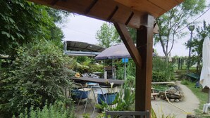 Un espacio al aire libre cubierto con una mesa y sillas, rodeado de abundante vegetación y un pequeño estanque.