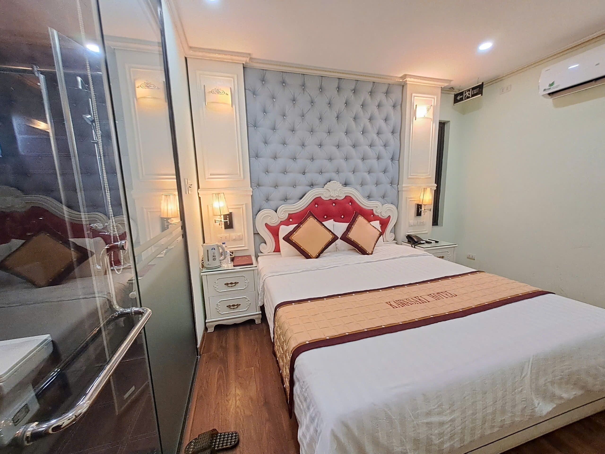 Habitación de hotel con una cama grande, una mesita de noche, un espejo y una puerta con panel de vidrio.