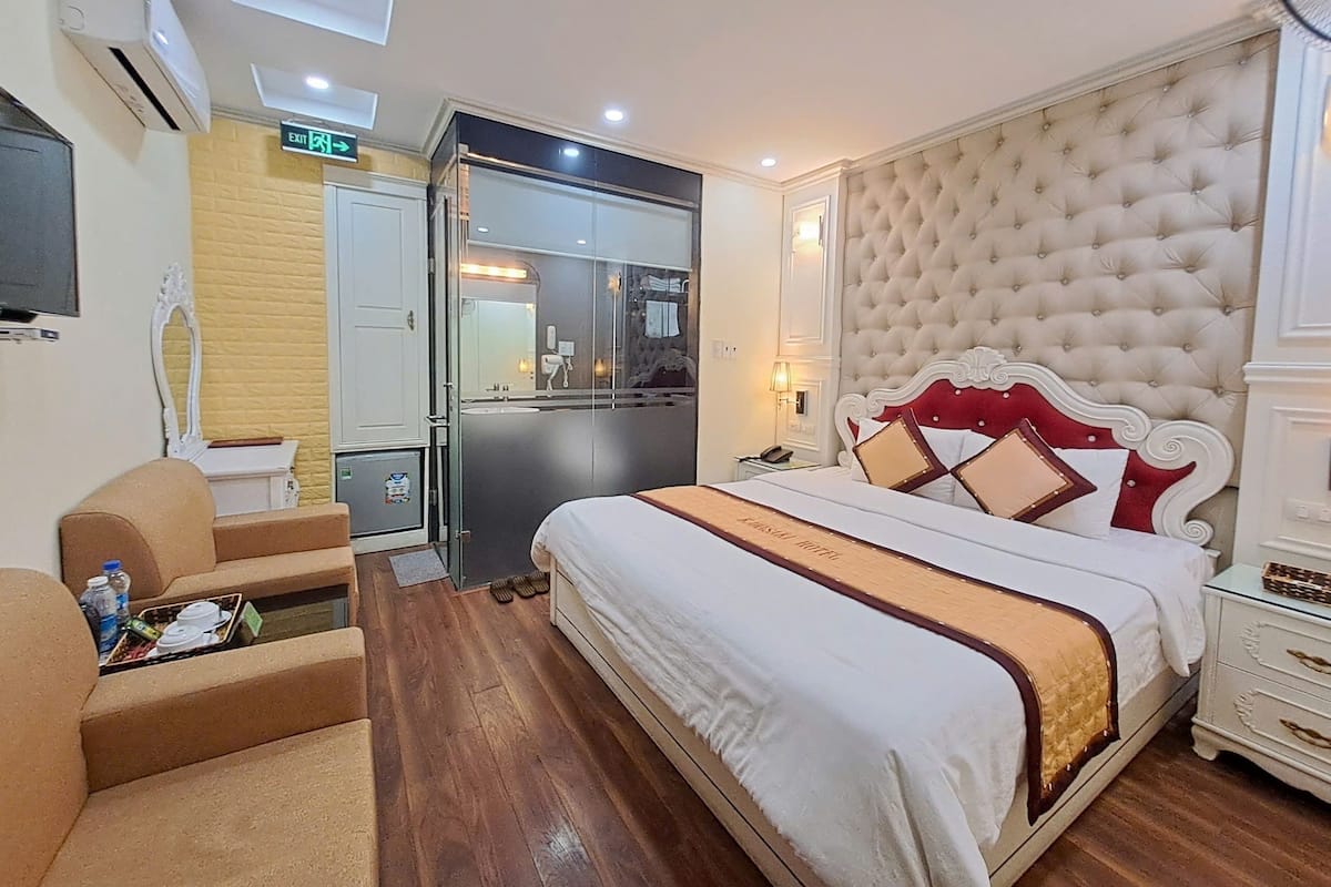 Ein Hotelzimmer mit einem großen Bett, einer Sitzecke mit Sofa und kleinem Tisch, einem Spiegel und einem an der Wand befestigten Fernseher.