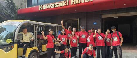 A group of people in red shirts posing in front of the Kawasaki Hotel.