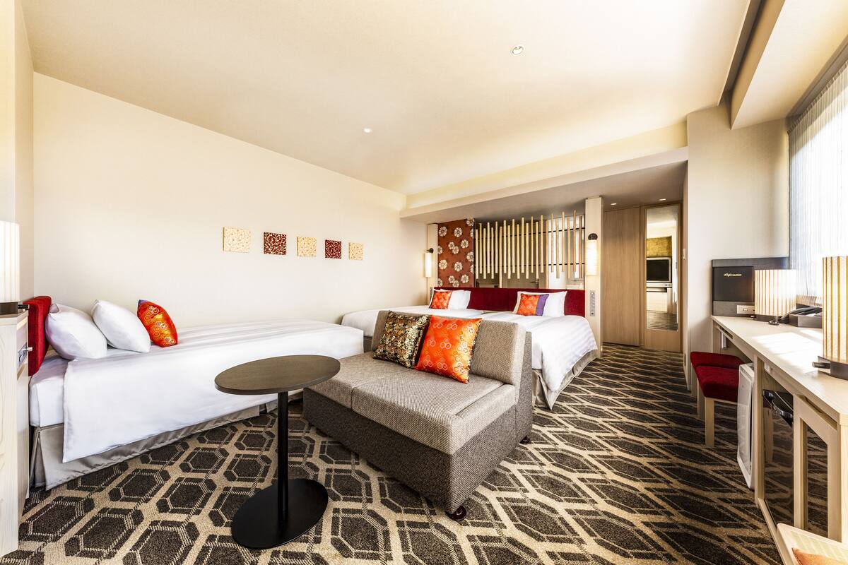 A hotel room with two beds, a sofa, a small table, and a TV.