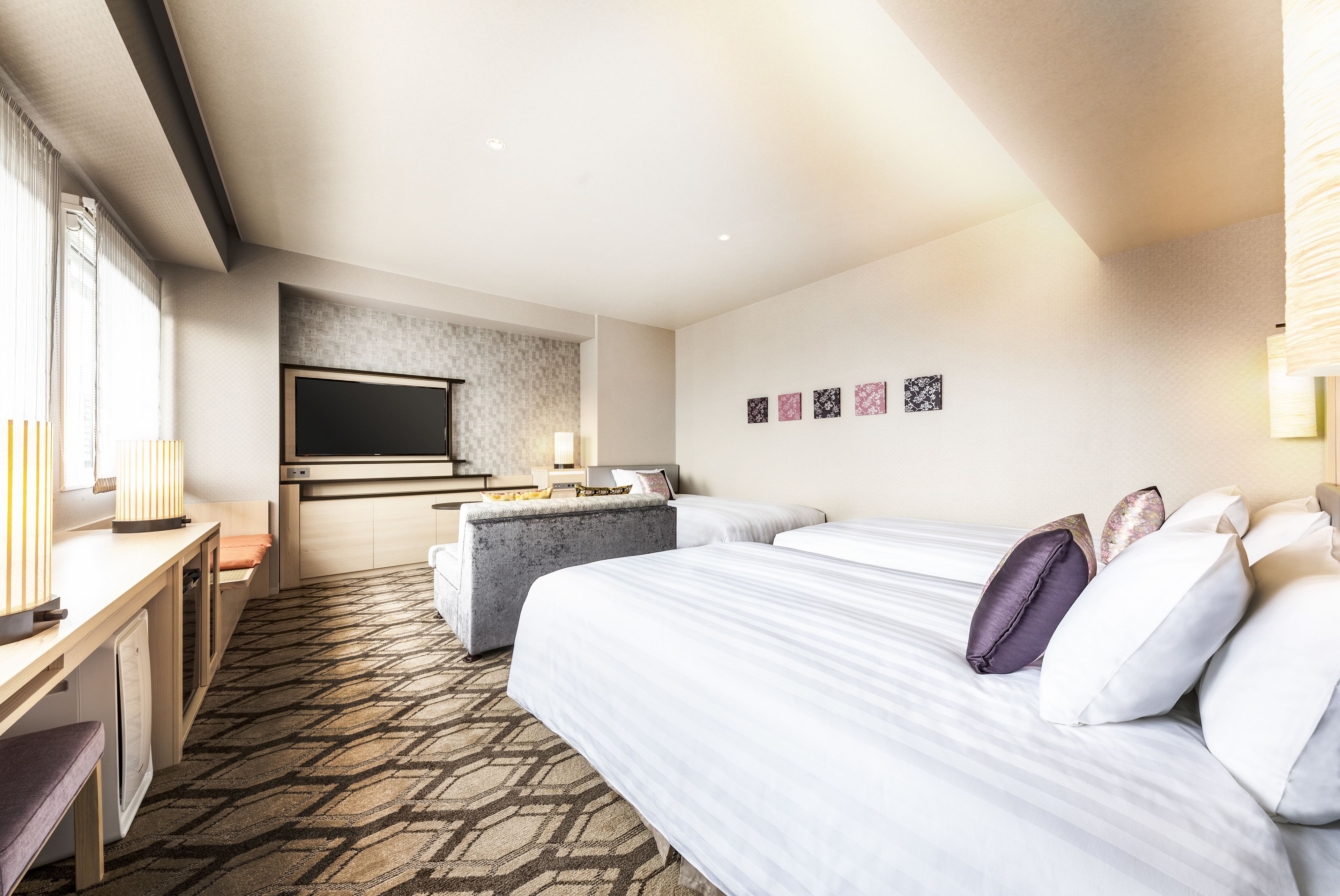 Habitación de hotel con cama, escritorio, televisión y una kitchenette pequeña.