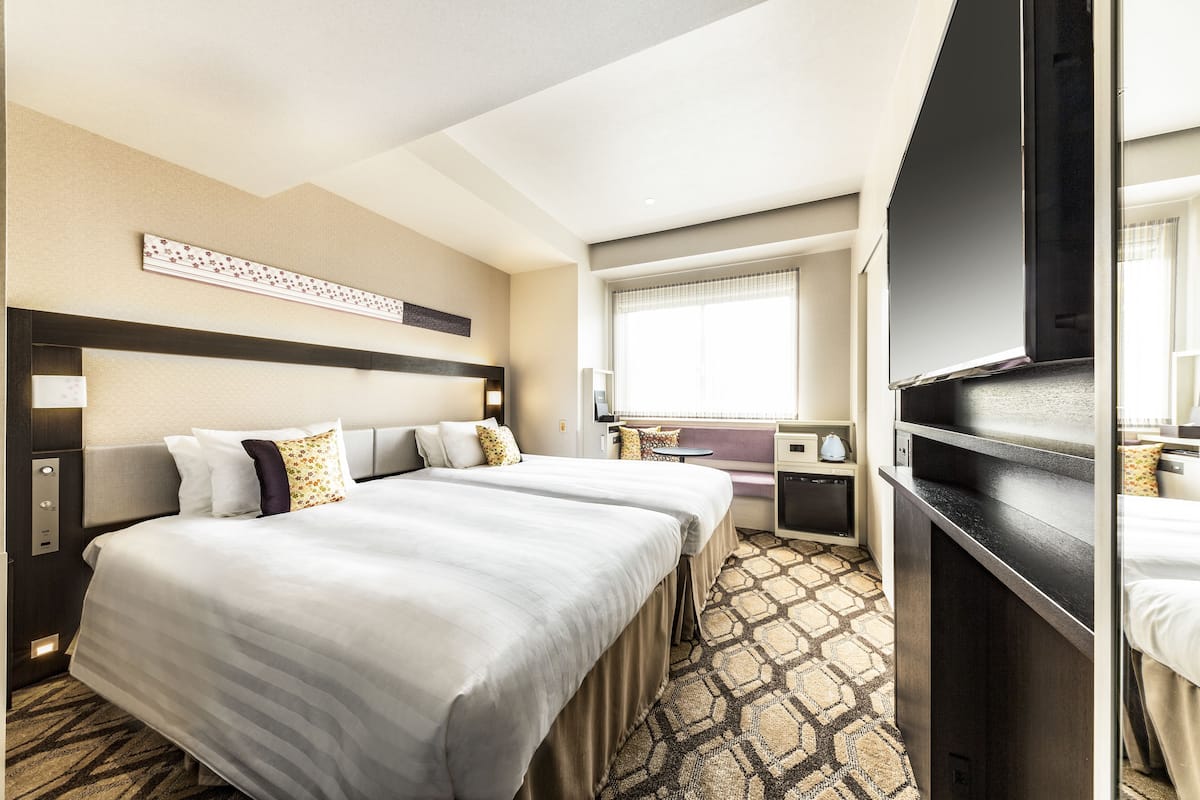 A hotel room with two beds, a large mirror, a flat-screen TV, and a window with curtains.