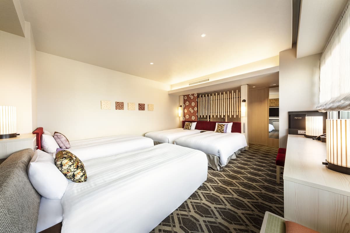 A hotel room with three beds, a desk, and a television.