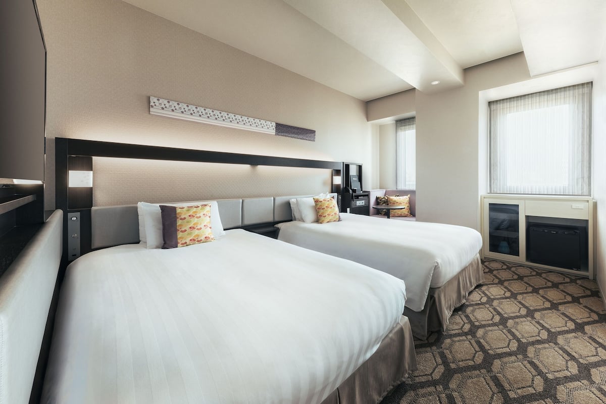 A hotel room with two beds, a desk, a chair, a small table, and a window with curtains.