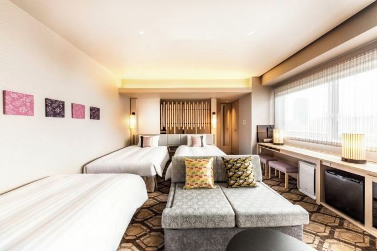 A hotel room with two beds, a sofa, a desk, and a TV.