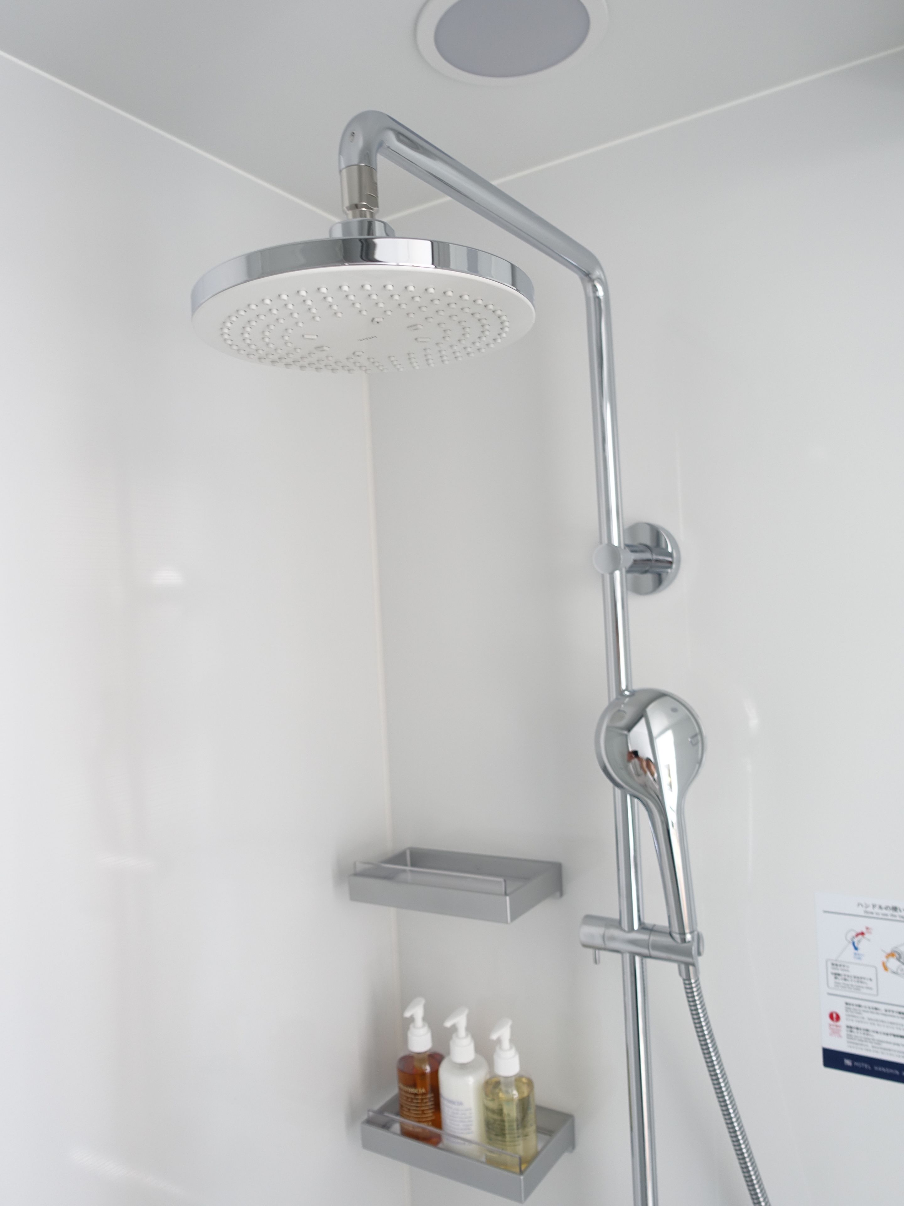 A modern shower with a handheld showerhead and a rain shower attachment. There are two shelves below the shower, holding toiletries.