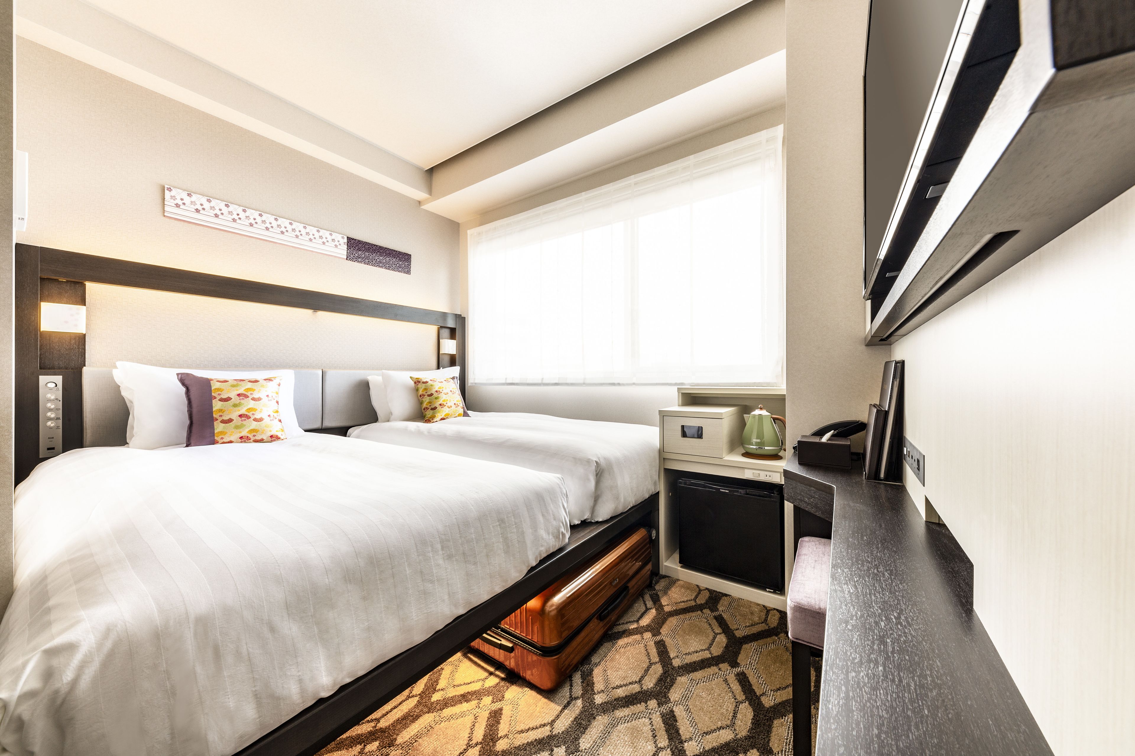 A hotel room with two beds, a desk, a television, and a window.
