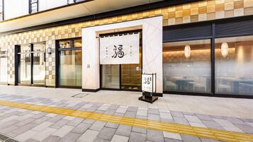 A building facade with a tiled entrance, a large sign with Japanese characters, and a clear pathway with tactile paving.