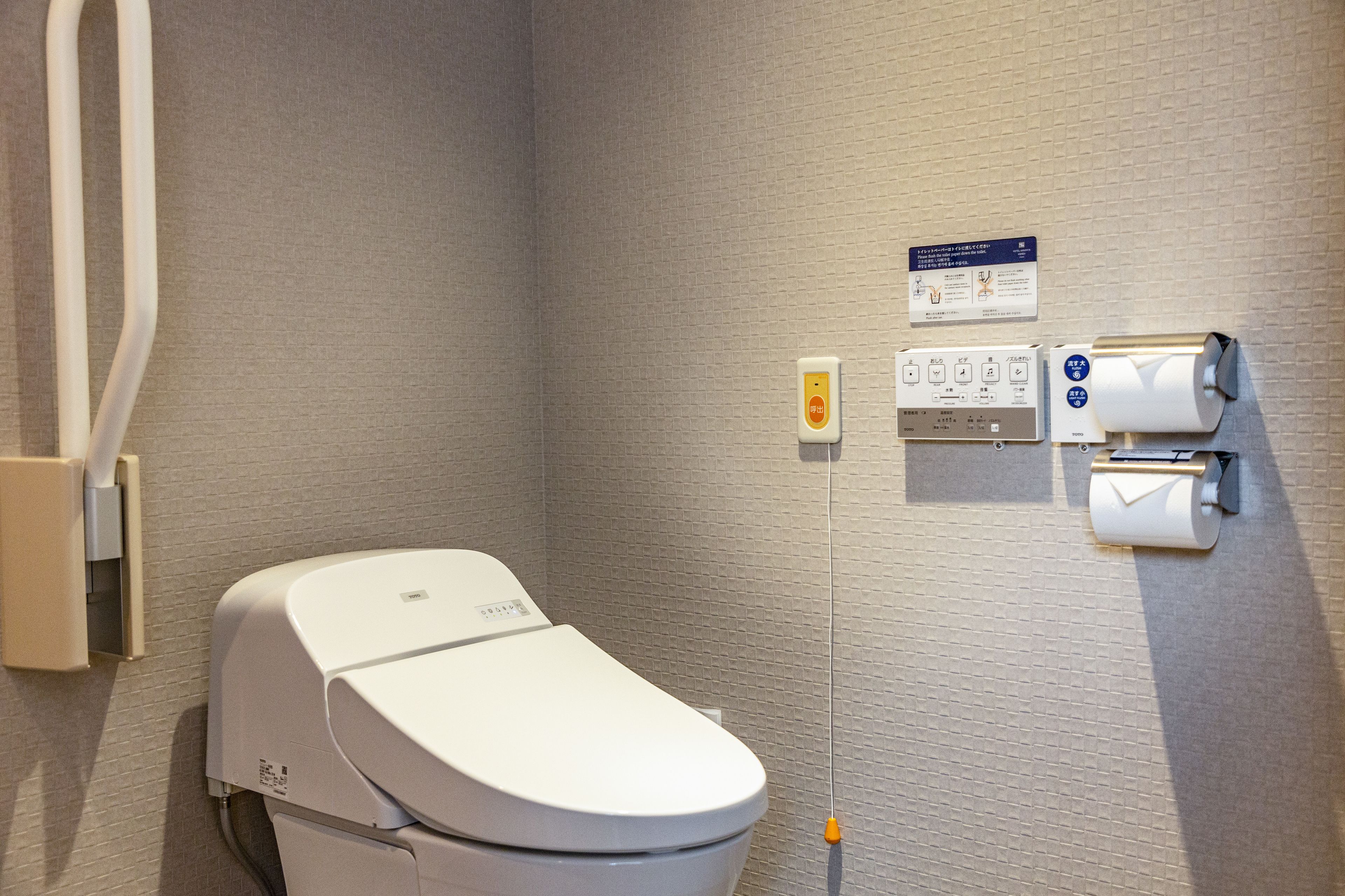 Une salle de bain moderne équipée de toilettes, d’un sèche-mains et d’un distributeur de serviettes en papier.