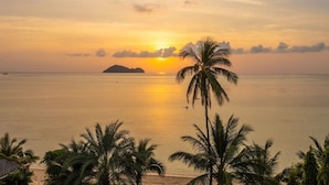 A sunset over a calm sea with a palm tree in the foreground and an island in the distance. - Baan Jai Dee Beach Front Hotel (Ko Pha-ngan)
