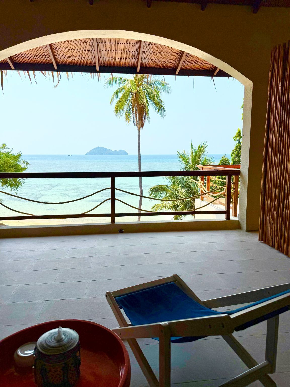 Een balkon met uitzicht op zee, een palmboom en een eiland in de verte.