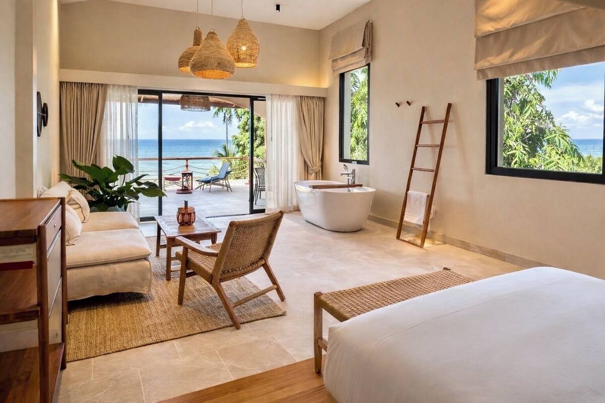 Une chambre dotée d’un grand lit, d’un coin salon avec un fauteuil, d’une baignoire et offrant une vue sur l’océan.