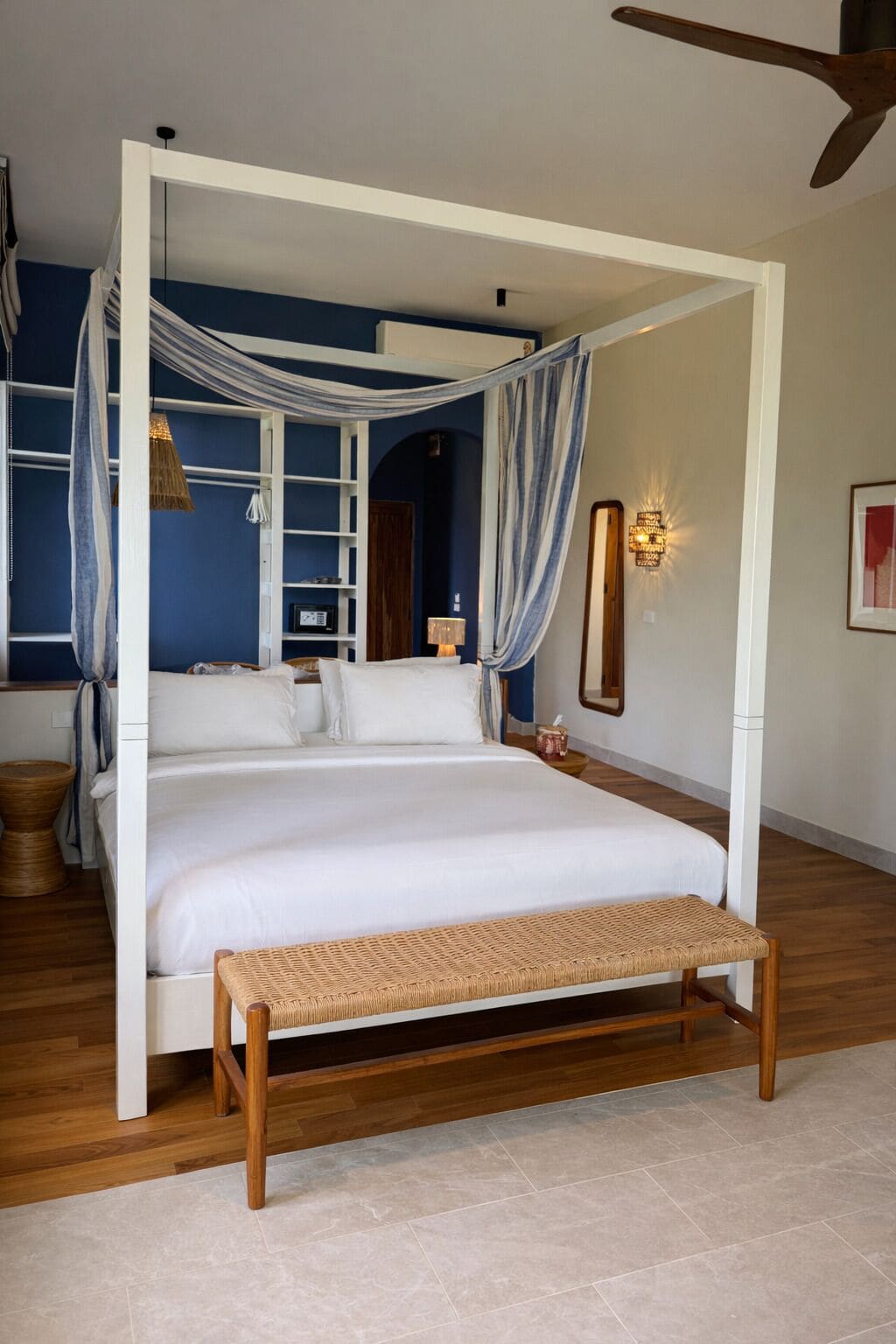 A four-poster bed with a canopy, a bedside table, a lamp, and a framed picture on the wall.