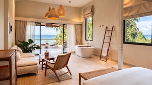 A spacious bedroom with a large bed, a sitting area with a table and chair, a bathtub, and a view of the ocean. - Baan Jai Dee Beach Front Hotel (Ko Pha-ngan)