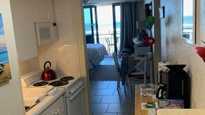 Una cocina compacta con estufa, microondas y vistas a la playa desde la puerta abierta.