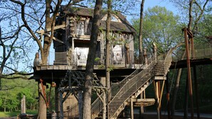 Una casa en un árbol con una escalera de madera y un puente colgante.