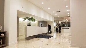 A modern hotel reception area with a white reception desk, a potted plant, and a glass partition. - Lincoln Rd & Collins Ave,  ROMANTIC 2 PERSON JACUZZI    (Miami Beach)
