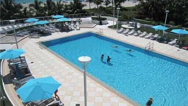A swimming pool with lounge chairs and umbrellas, surrounded by palm trees and a view of the ocean. - Lincoln Rd & Collins Ave,  ROMANTIC 2 PERSON JACUZZI    (Miami Beach)