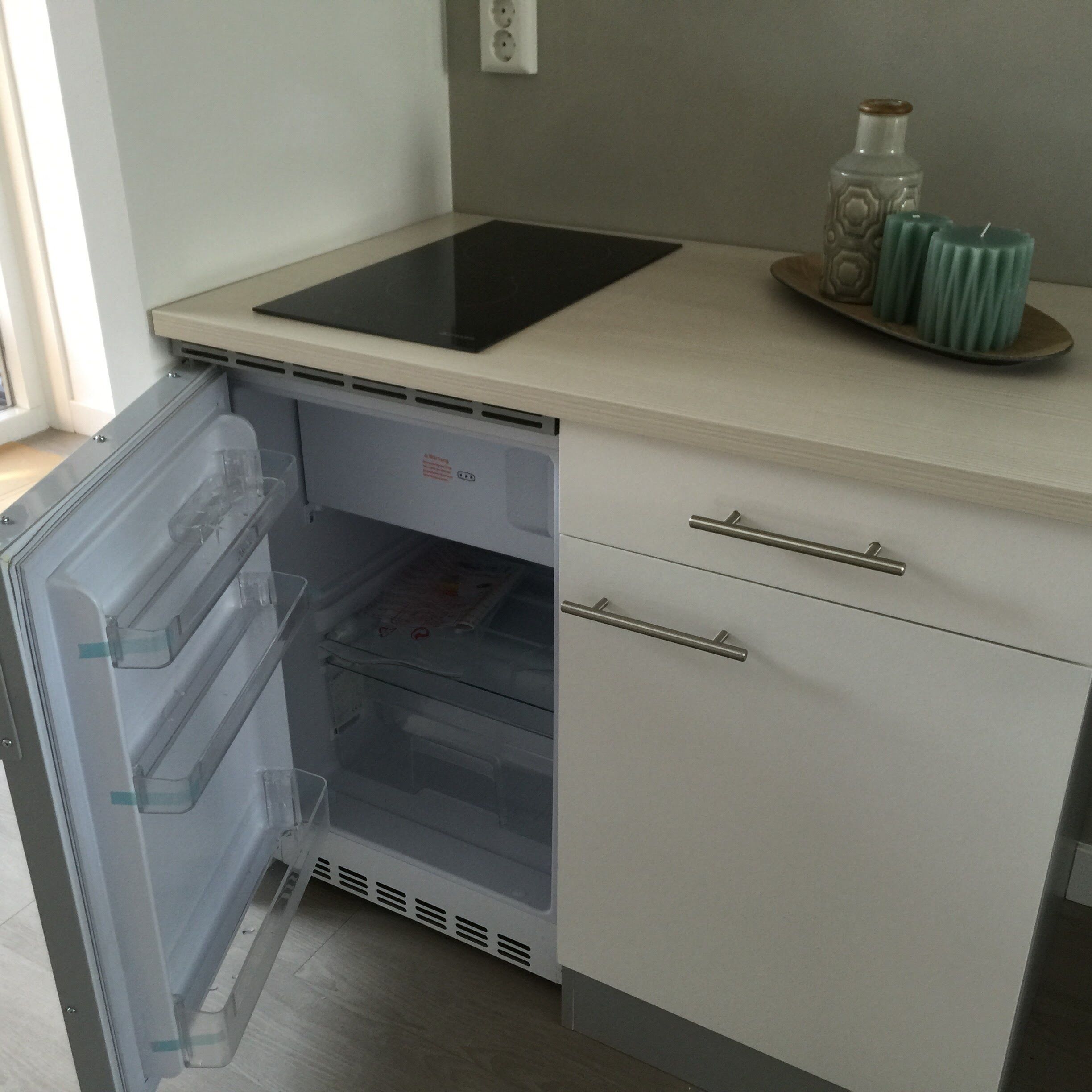 A kitchen with a built-in refrigerator, a microwave, and a small countertop with a tea set.