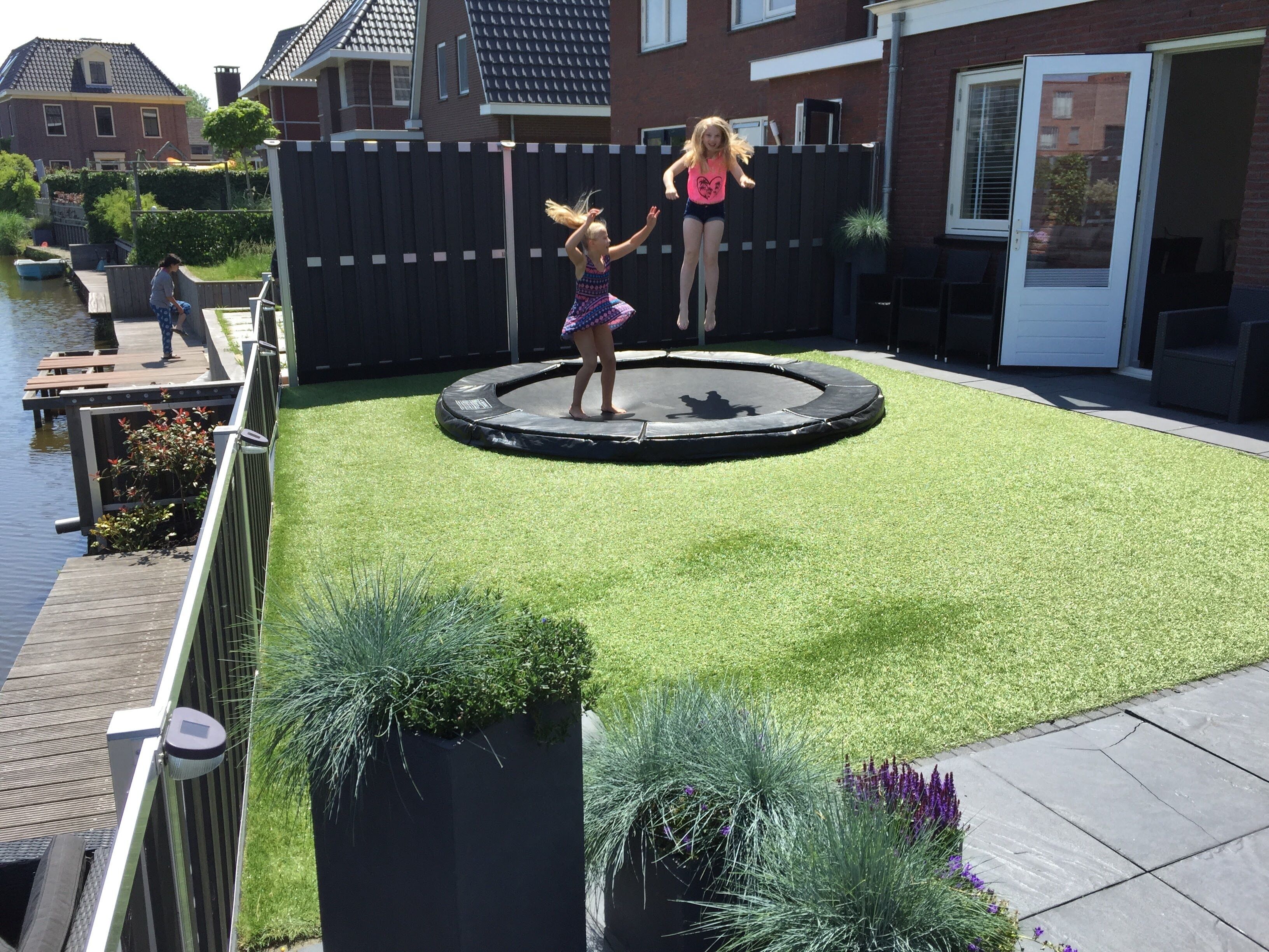 A backyard with a trampoline, artificial grass, and a wooden deck.