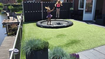 A backyard with a trampoline, artificial grass, and a wooden deck.