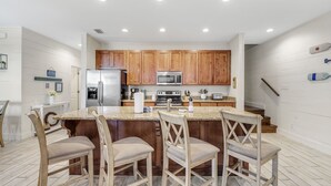 A modern kitchen with wooden cabinets, a stainless steel refrigerator, a microwave, and a granite countertop. - Modern True Blue: Gulf Shores Escape w/ Deeded Beach Access, Pool & Beach Gear! (Gulf Shores)