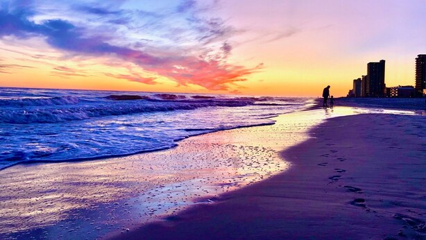 A beach with waves and a sunset. There are buildings in the background. - Modern True Blue: Gulf Shores Escape w/ Deeded Beach Access, Pool & Beach Gear! (Gulf Shores)