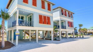 A two-story beachfront house with a balcony, a sign indicating a location, and a clear blue sky. - Modern True Blue: Gulf Shores Escape w/ Deeded Beach Access, Pool & Beach Gear! (Gulf Shores)