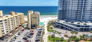A hotel with a pool, beach view, and parking lot.