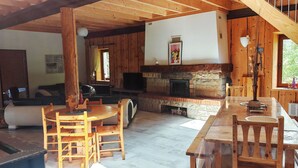 Een gezellig chaletinterieur met een houten eettafel, stoelen, een bank en een open haard.