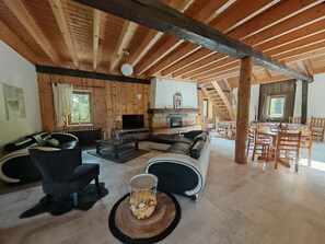 Un vaste salon doté d’un plafond en bois, d’une cheminée, d’un coin repas et d’un escalier menant à l’étage supérieur.