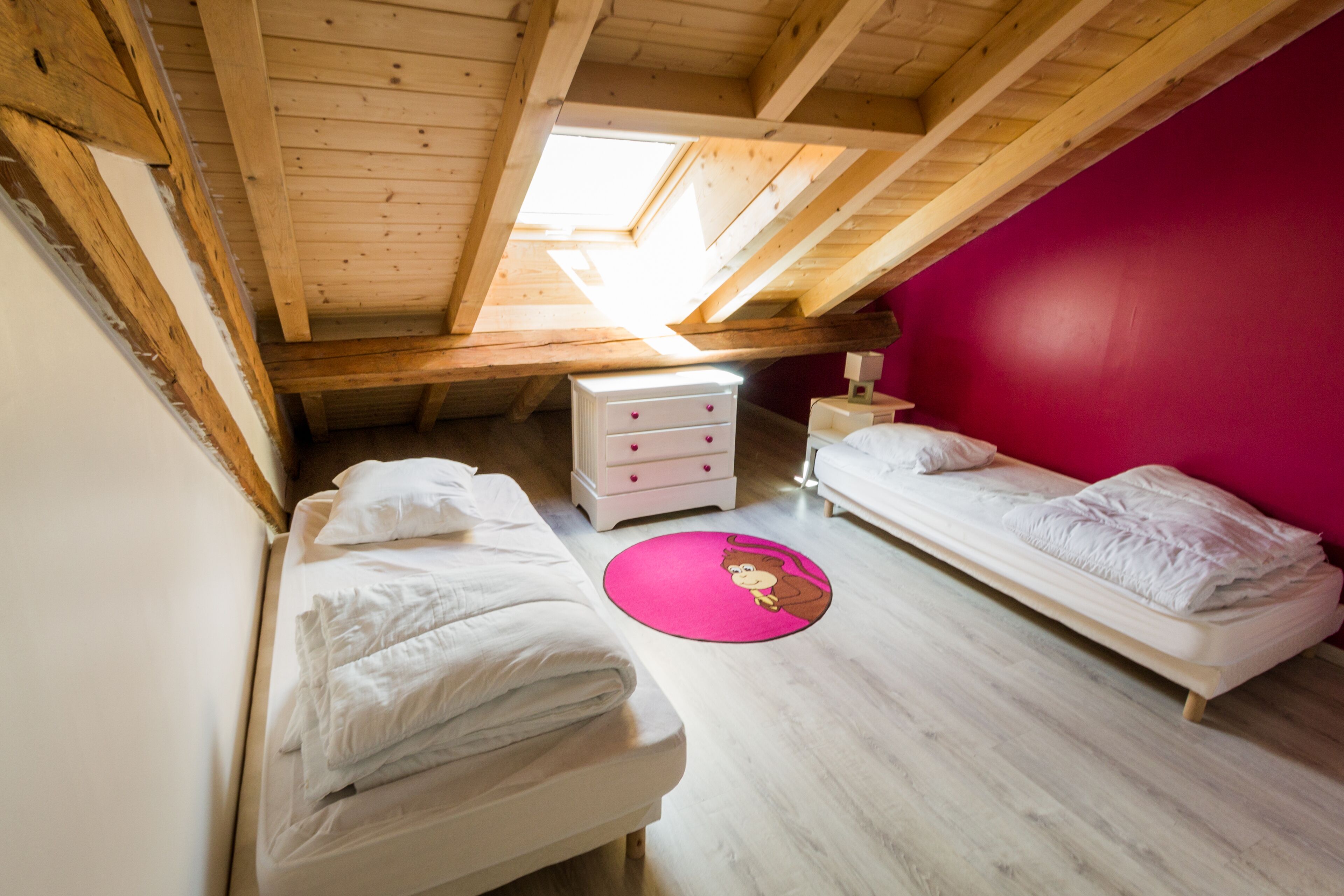 Une chambre avec deux lits, un mur rose et une lucarne.
