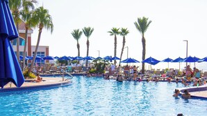 Ein Pool mit Liegestühlen und Sonnenschirmen, umgeben von Palmen.